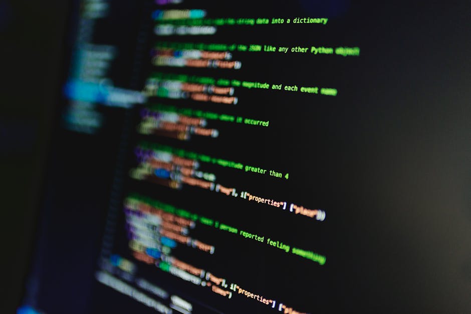 The image shows a close-up of a computer screen displaying lines of coloured programming code with syntax highlighting in green, blue, purple, and orange on a black background. The text appears slight